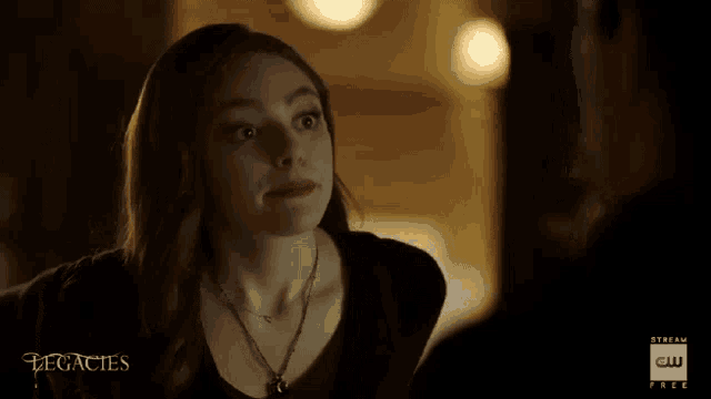a woman wearing a necklace and a black shirt is looking at a man in a dark room .