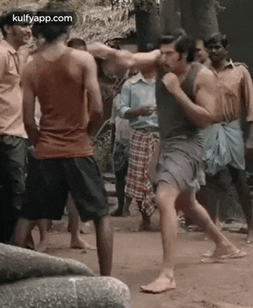a group of men are fighting each other on a dirt road in front of a crowd .