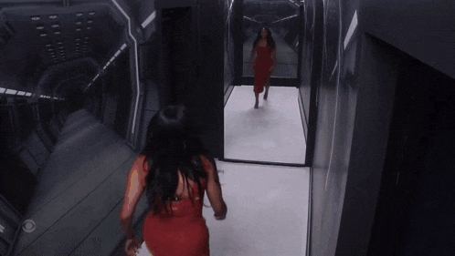 a woman in a red dress is dancing in a hallway with a cbs logo on the wall