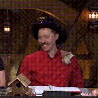 a man wearing a cowboy hat and a red shirt is sitting at a table with a birdhouse .
