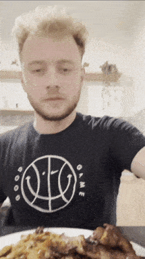 a man wearing a black shirt that says game is eating a plate of food