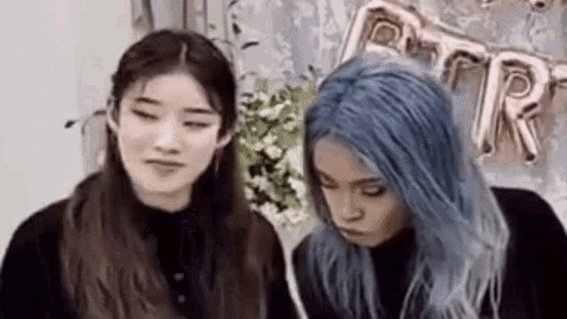 two girls with blue hair are sitting next to each other and looking at each other .