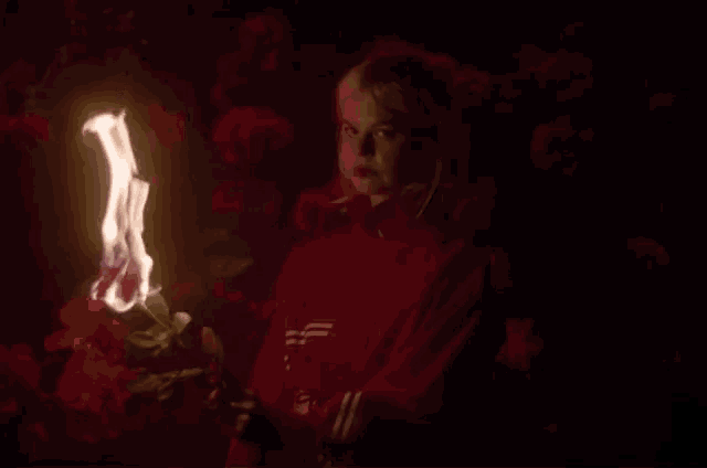 a woman in a red adidas sweatshirt holds a burning flower