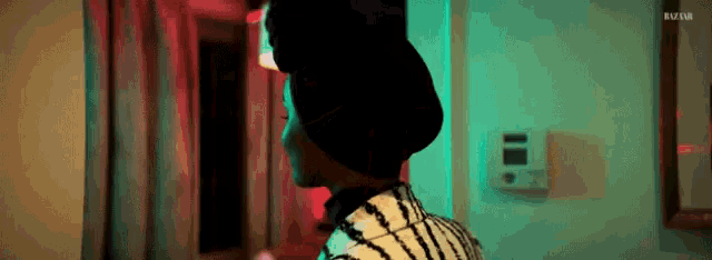 a woman in a black hat is standing in a hallway with a red light behind her .