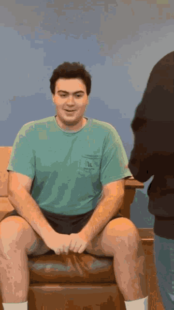 a man in a green t-shirt is sitting on a couch
