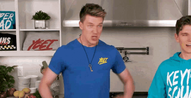 a man in a blue yeet shirt stands next to another man in a blue hoodie