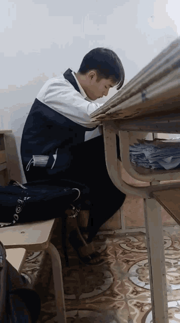 a boy sits at a desk with a stack of papers on top of him