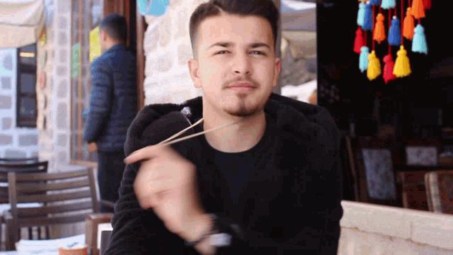 a man wearing a black sweatshirt is sitting at a table eating something