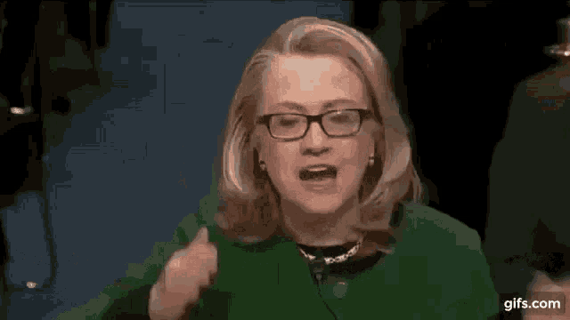 hillary clinton is wearing glasses and a green jacket and talking .
