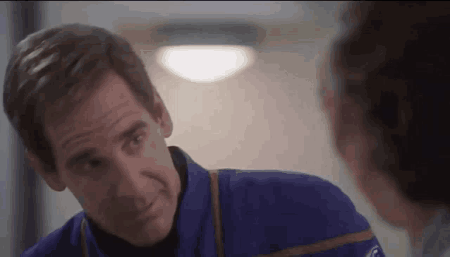 a man in a blue uniform is smiling and looking at another man .