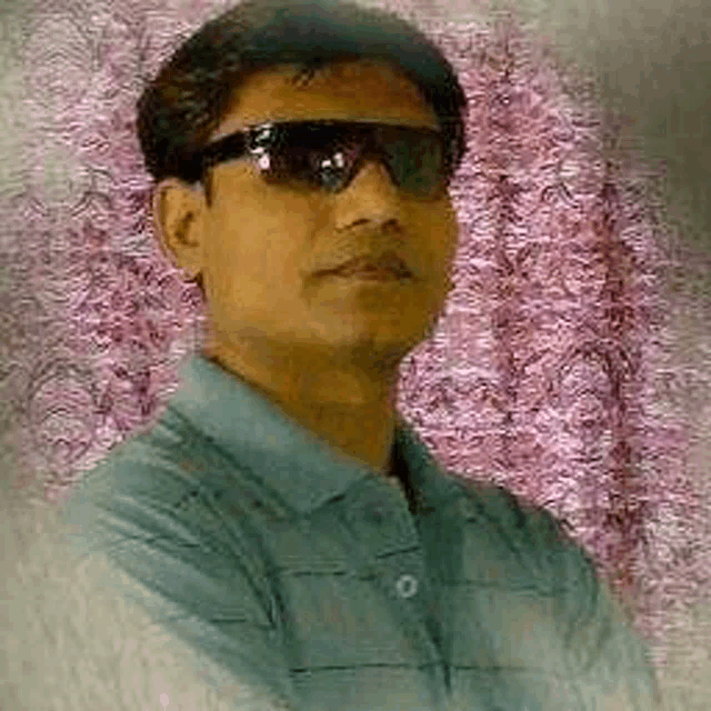 a man wearing sunglasses and a blue shirt is standing in front of a pink wall .