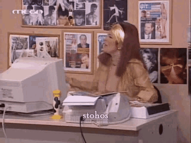 a woman is sitting at a desk in front of a computer with the word stohos on the screen .