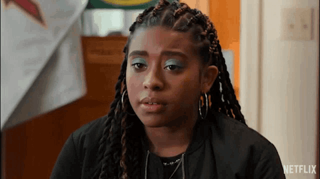 a young girl with dreadlocks and blue eye shadow is wearing a black jacket and hoop earrings .