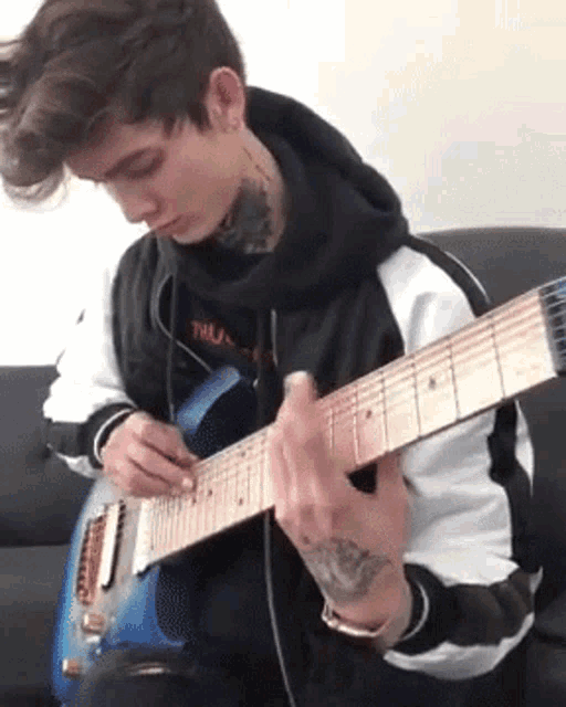 a young man is sitting on a couch playing a blue electric guitar .