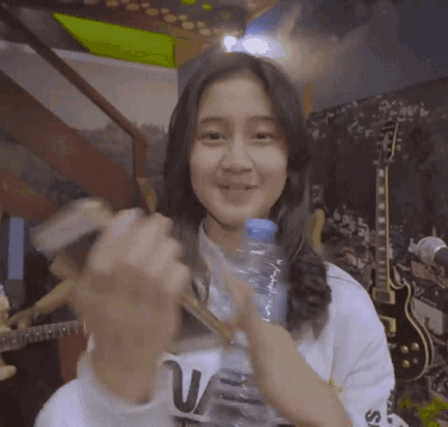 a girl holding a bottle of water in front of a guitar