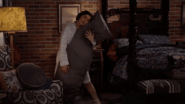 a woman is holding a pillow in a bedroom with a brick wall