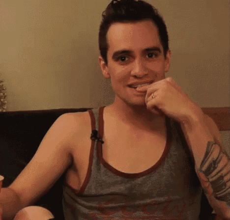a man in a tank top is sitting on a couch with his hand on his chin .