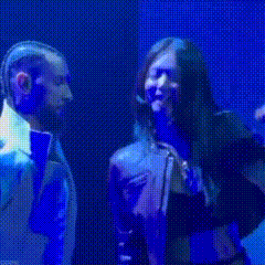 a woman with long hair is singing into a microphone on a stage in front of a blue background .