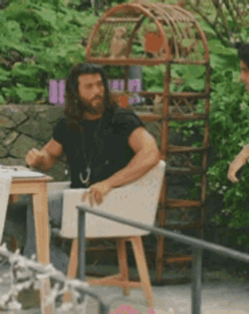 a man with a beard is sitting in a chair in front of a bird cage