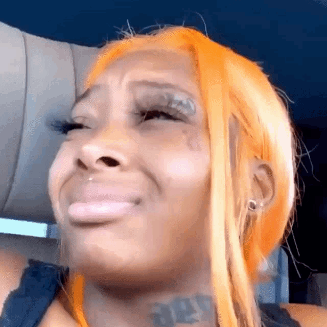 a woman with orange hair and a tattoo on her neck is making a funny face while sitting in a car .