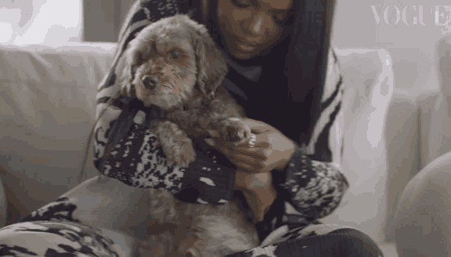 a woman sitting on a couch holding a small dog with vogue written on the bottom right