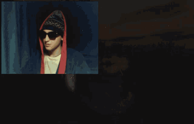 a young man wearing sunglasses and a hooded jacket is giving a middle finger