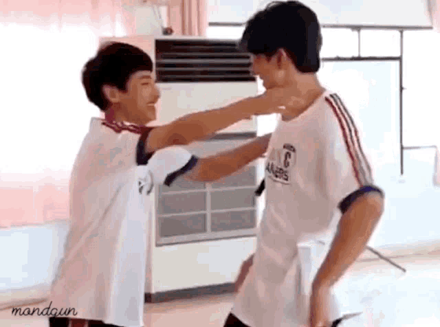 two young men are standing next to each other in a room and fighting .