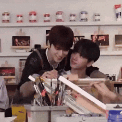 two young men are sitting next to each other in front of a table with brushes .