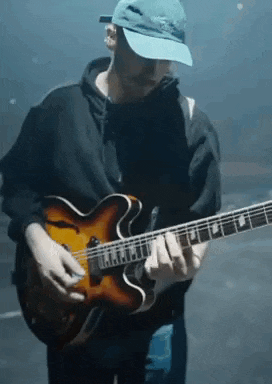 a man wearing a blue hat is playing a guitar in a dark room .