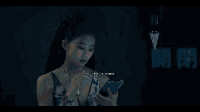 a woman with dreadlocks looks at her cell phone in front of a sign with chinese characters