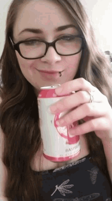 a woman wearing glasses holds a can of raspberry juice