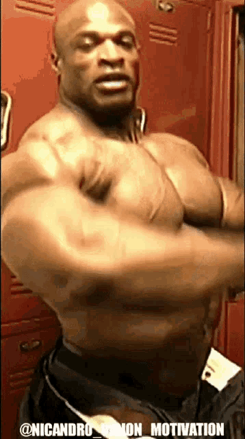 a man flexes his muscles in front of a red locker with the words @nicandro on the bottom right