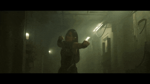 a woman in a black outfit is flexing her muscles in a dark hallway