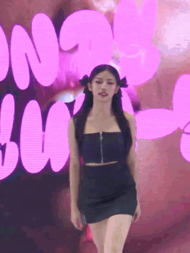 a woman in a black dress is standing in front of a pink background with balloons .