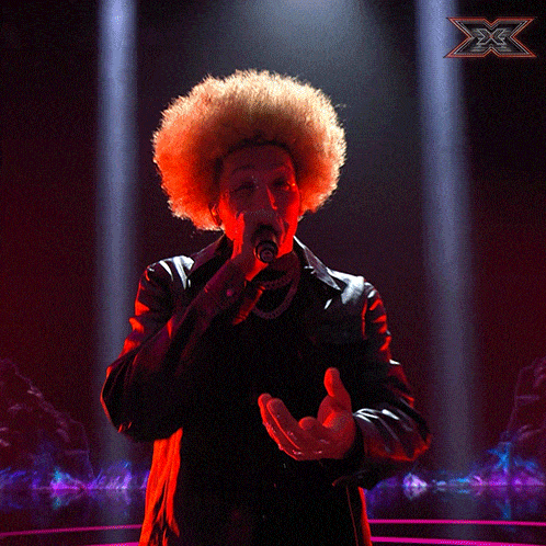 a woman with an afro singing into a microphone with a x on the bottom right
