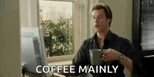 a man is drinking coffee while sitting at a desk in front of a computer monitor .