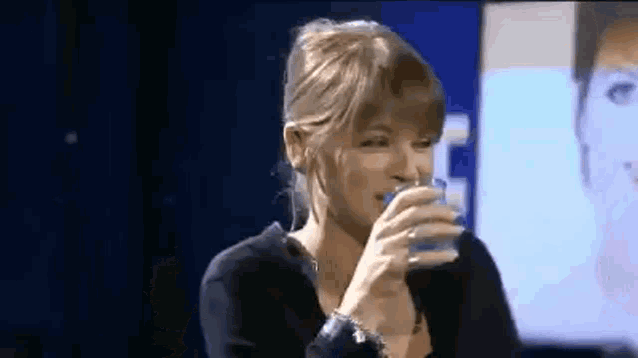 a woman is drinking a glass of water in front of a television .