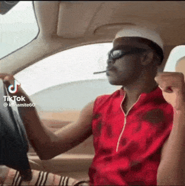 a man is driving a car and smoking a cigarette while wearing sunglasses and a hat .