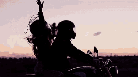 a man and a woman riding a motorcycle with their arms in the air