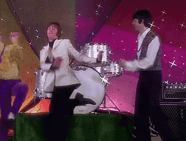 a man in a white suit is dancing in front of a ludwig drum .