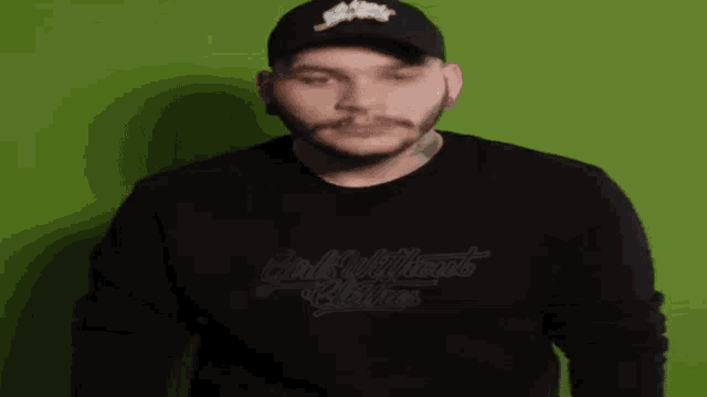 a man wearing a hat and a black sweater is standing in front of a green background .