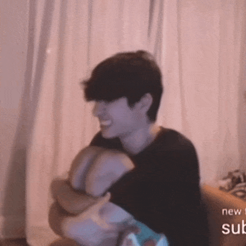 a man sits on a couch with his arms around another man 's waist with the words new sub visible on the bottom