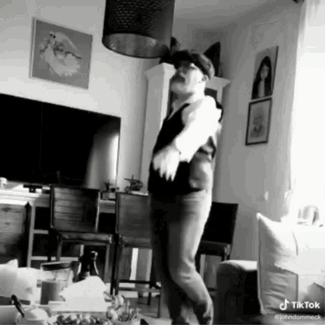 a man in a suit and hat is dancing in a living room with a tv in the background .