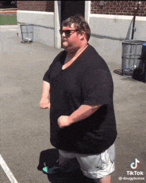 a fat man wearing sunglasses and a black shirt is standing in front of a brick building ..