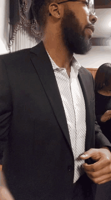 a man with a beard is wearing a black jacket and a white shirt