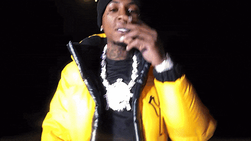 a man wearing a yellow jacket and a black beanie smoking a cigarette