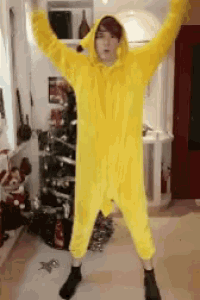 a person in a yellow onesie is standing in front of a christmas tree with their arms in the air