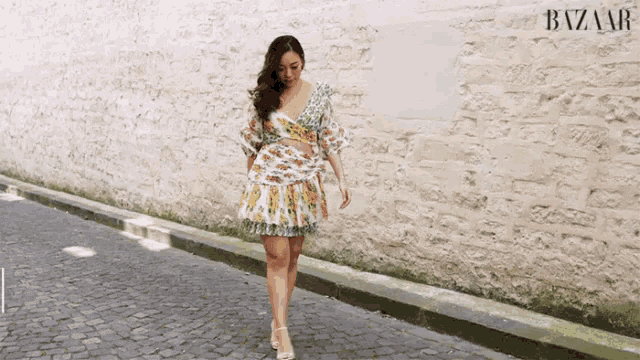 a woman in a floral dress walks down a cobblestone street