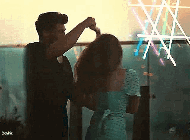 a man is brushing a woman 's hair in front of a neon sign that says sophie .
