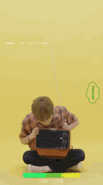 a young man is sitting on the floor holding a small television with bang ye written on the bottom